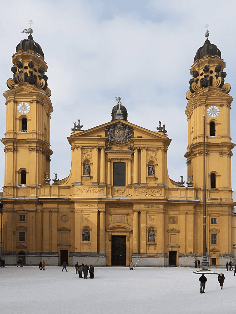 Golden Baroque church with twin towers and ornate facade in a European city square.