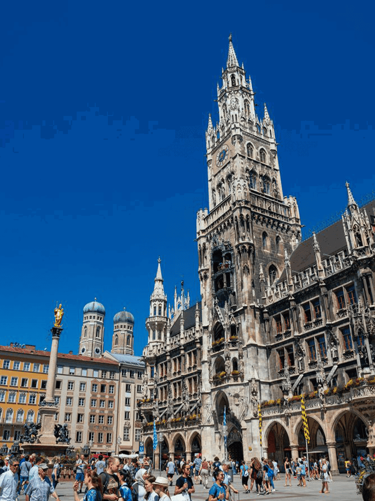 Historic Munich Glockenspiel tower, iconic architecture, tourists at Marienplatz square in Germany.