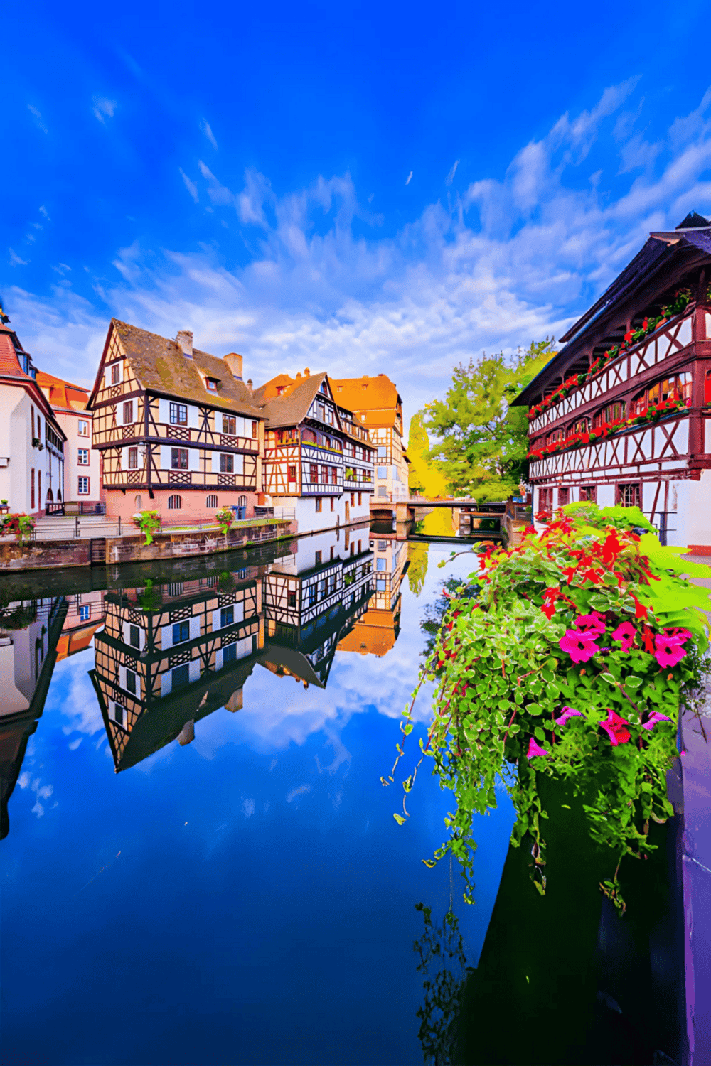 Charming European village with colorful half-timbered houses reflected in a tranquil canal, perfect for travel planning and directions.
