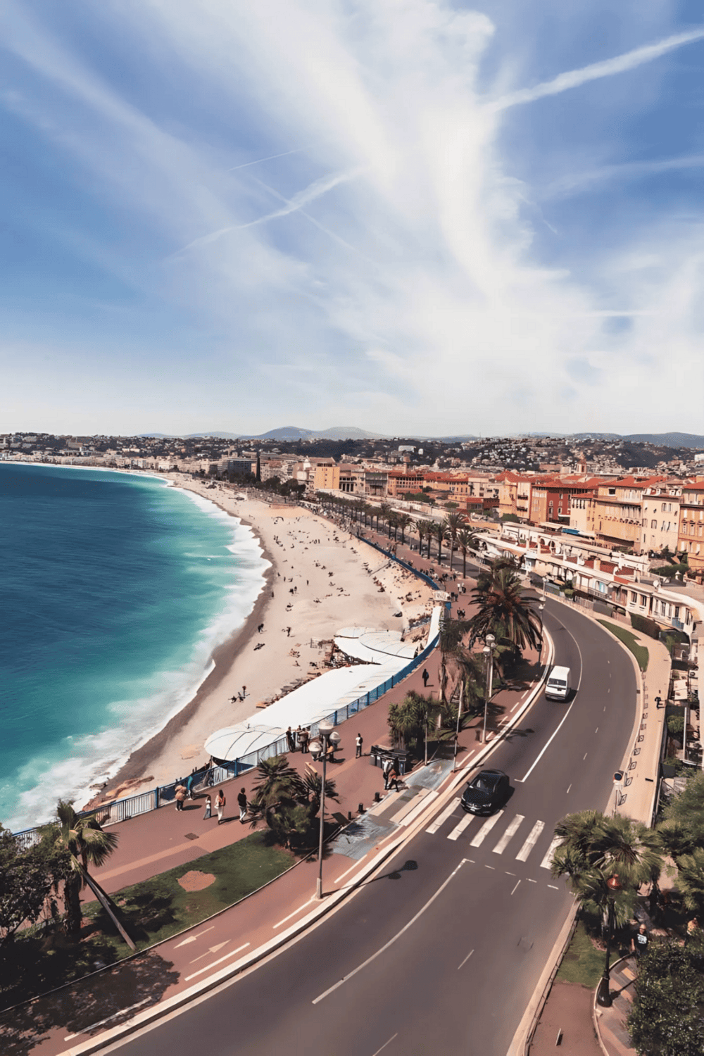 Vibrant coastal cityscape with palm-lined promenade, sandy beach, and turquoise ocean views under a bright blue sky.