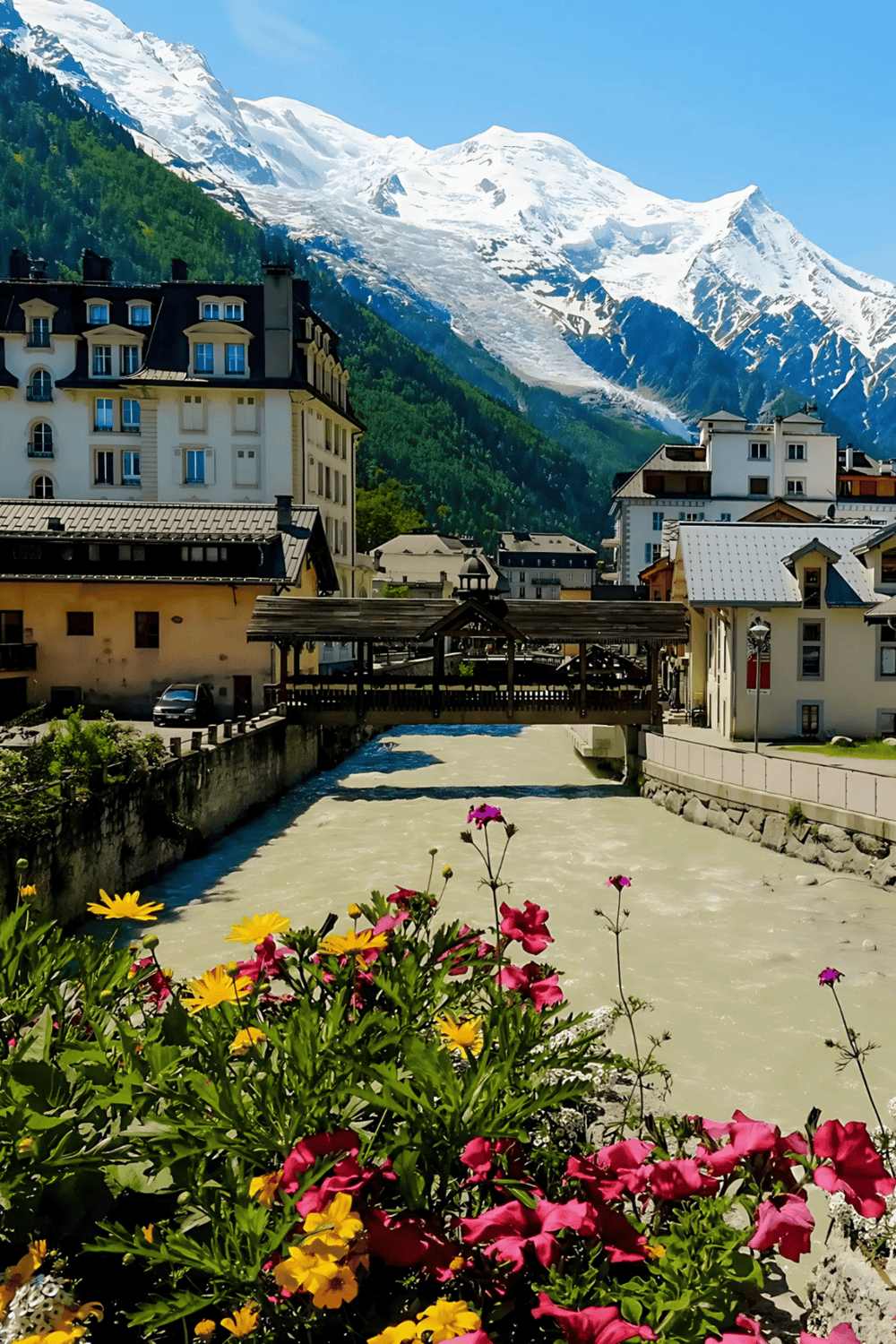 Snow-capped mountains and charming alpine village in Switzerland with a river and colorful flowers.