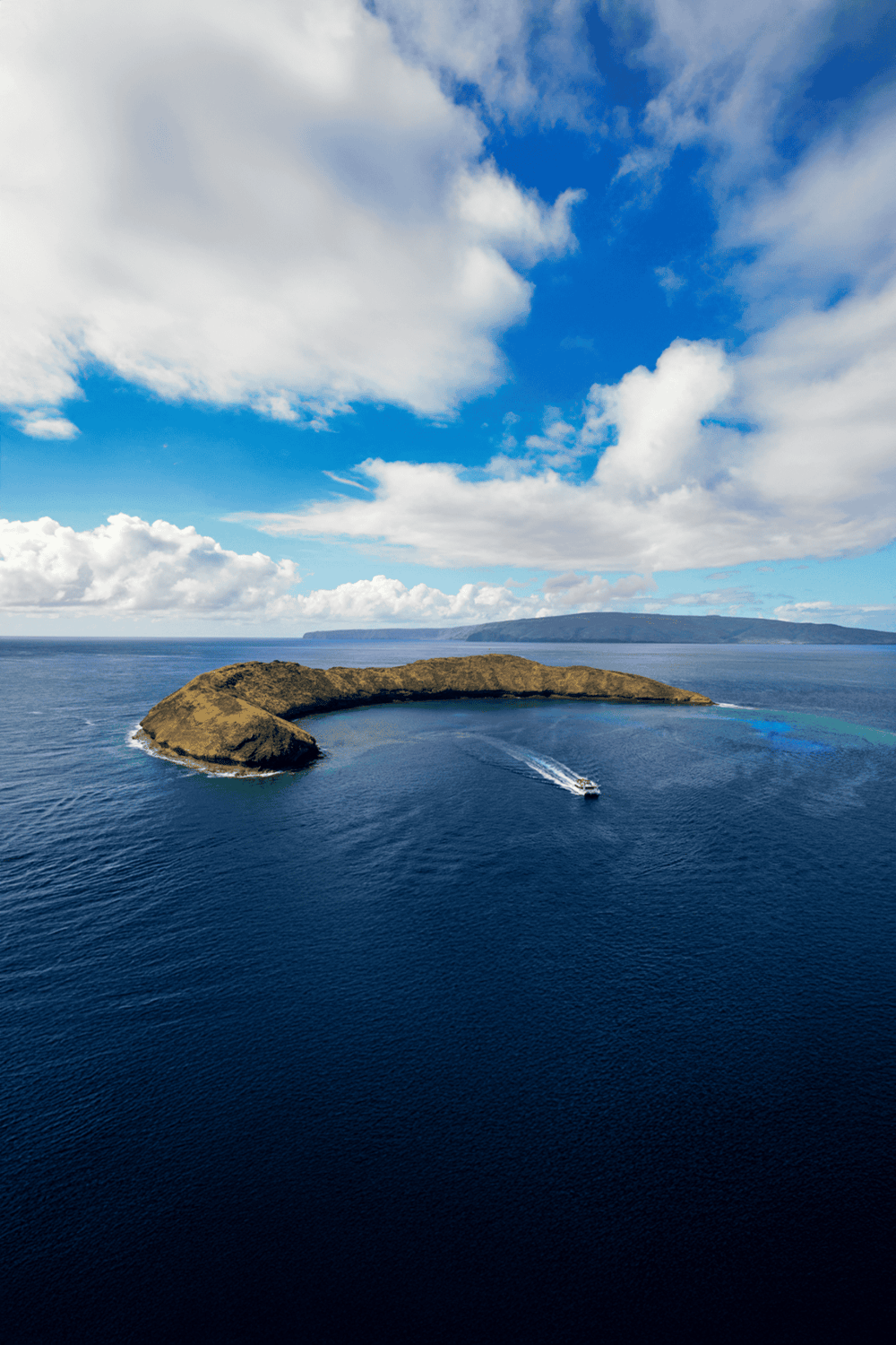 Secluded island with boat navigating around, scenic ocean views, and vibrant blue sky.
