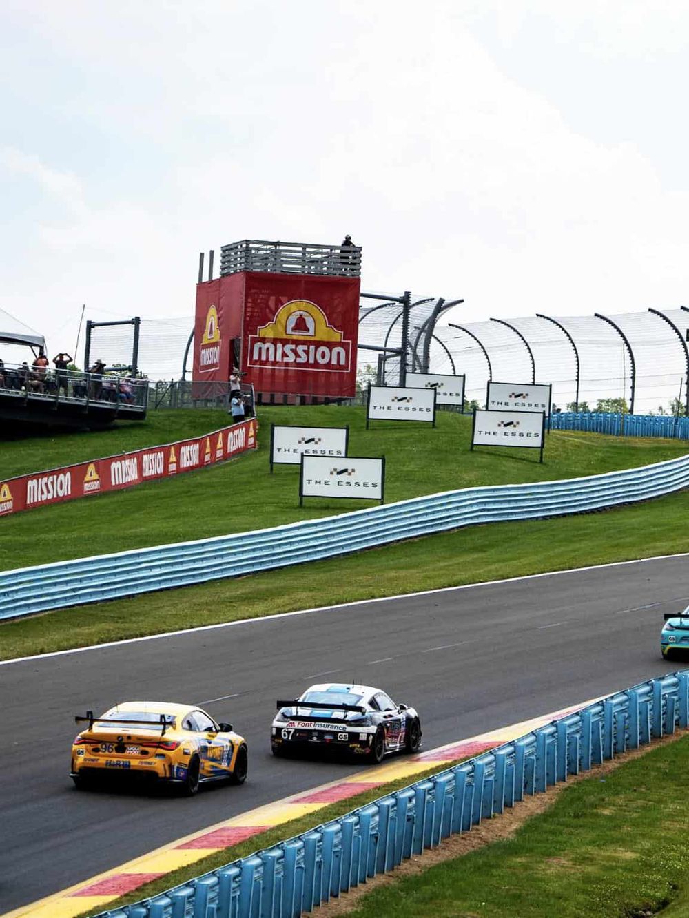 Race cars on a track with branding and sponsorship banners at a motorsport event.