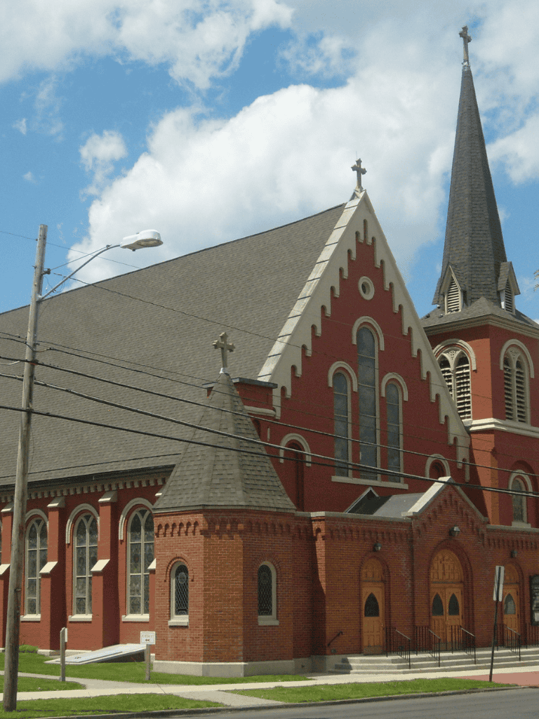 Historic red brick church with steeples and stained glass windows, located in a downtown area with power lines.