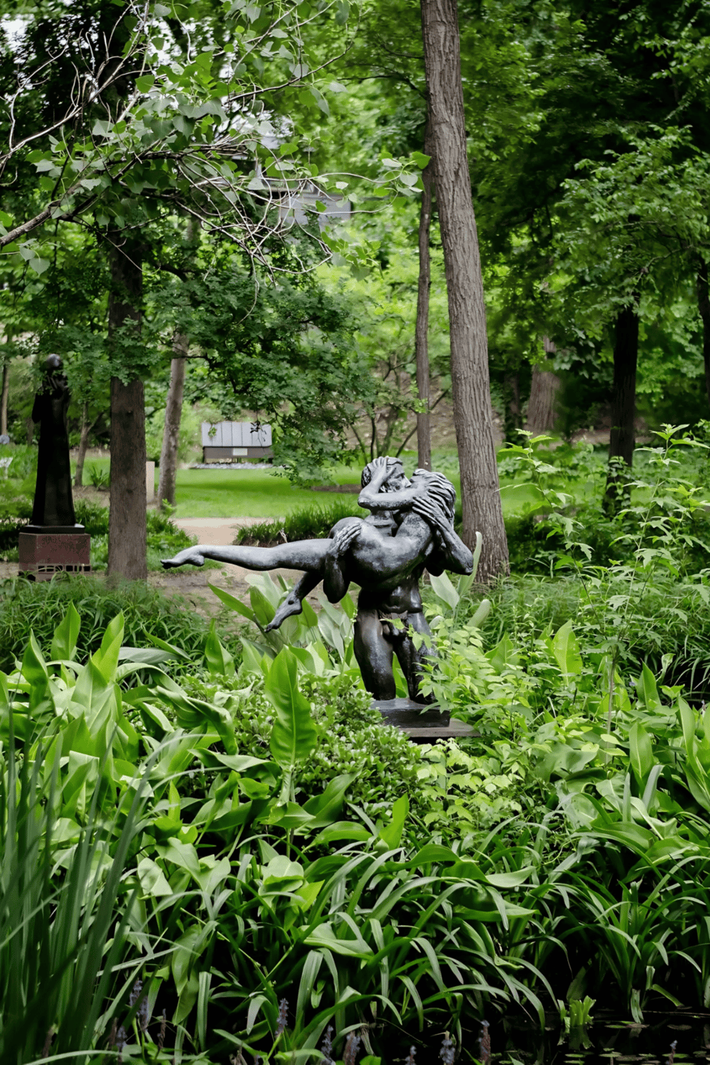 A lush green park with a classical sculpture of a mythical creature among trees and vibrant foliage.