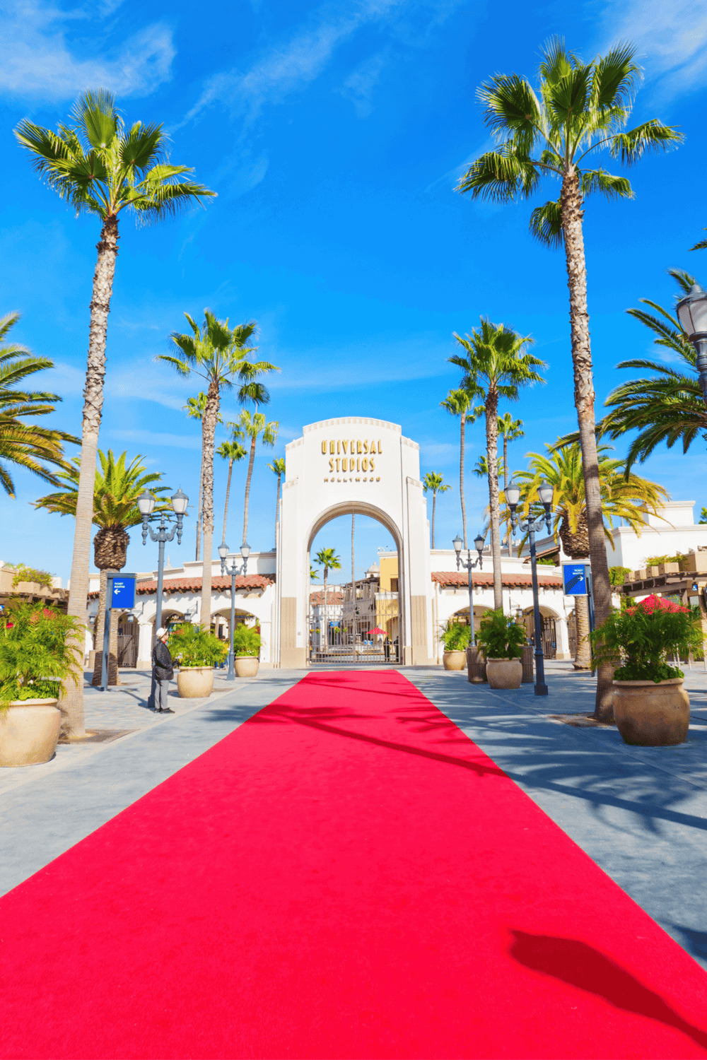 Vibrant entrance to Universal Studios Hollywood with a red carpet, palm trees, and clear blue sky.