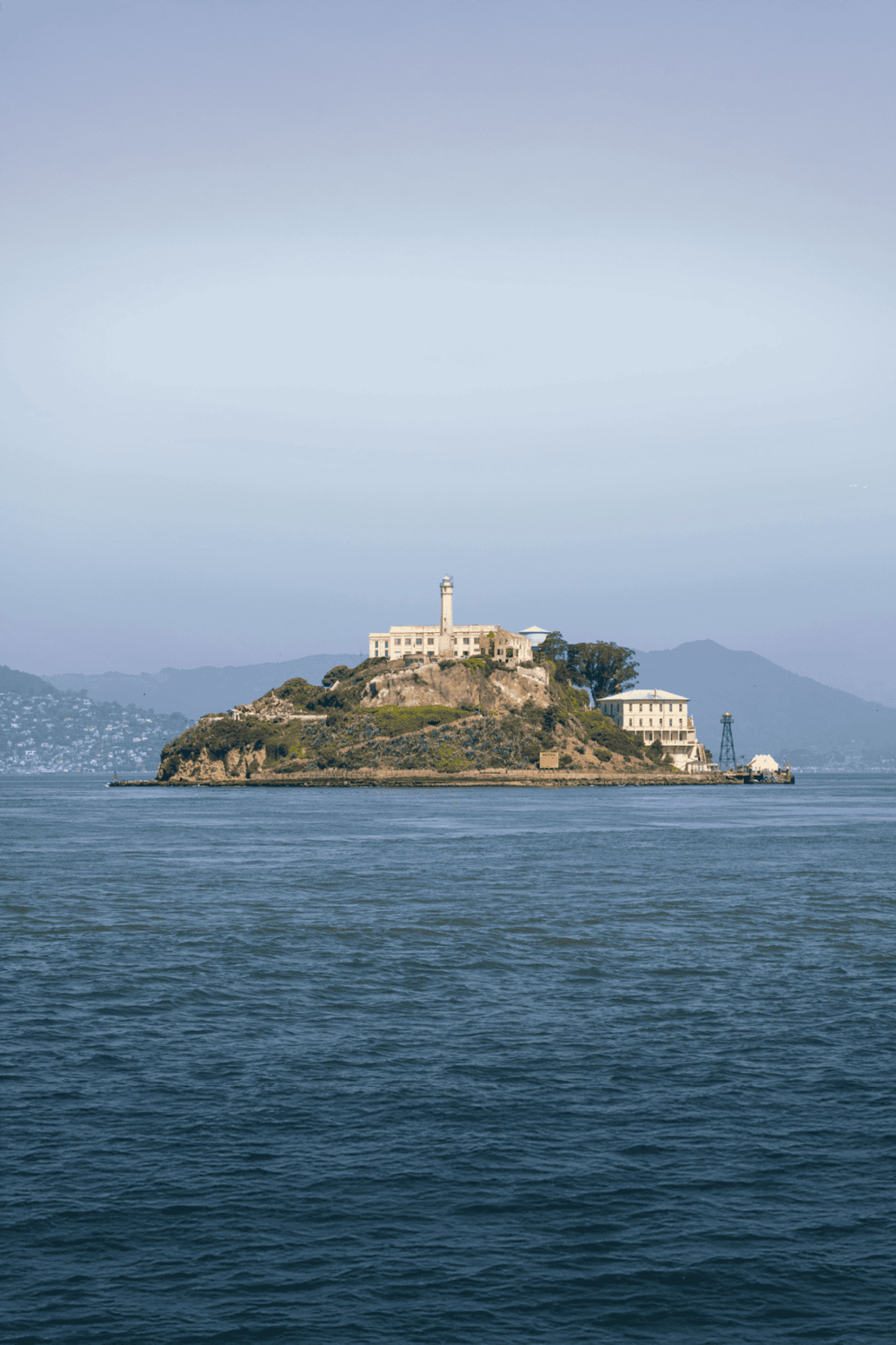 Lighthouse on Alcatraz Island in San Francisco Bay with city and mountain background.