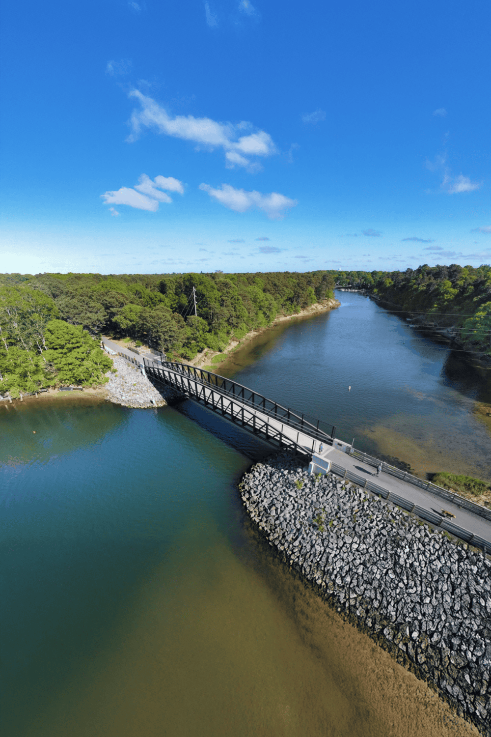 Spanning bridge over a river surrounded by lush greenery and clear blue sky, perfect for navigation and directions.