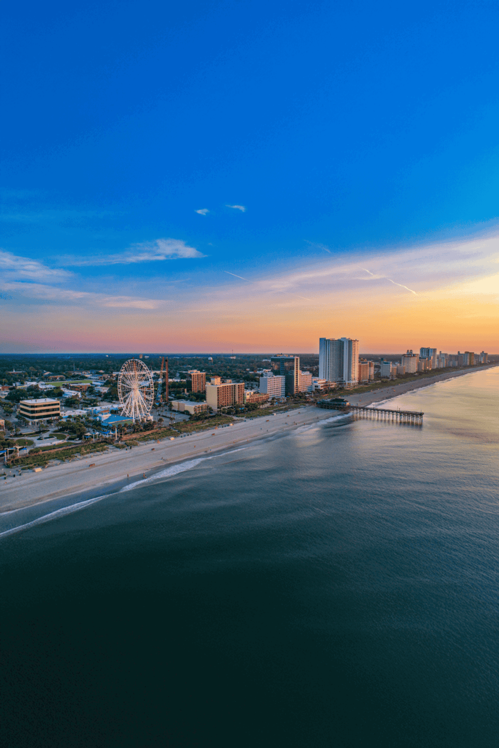 Beachside cityscape at sunset with Ferris wheel and coastal skyline, perfect for travel and tourism SEO.
