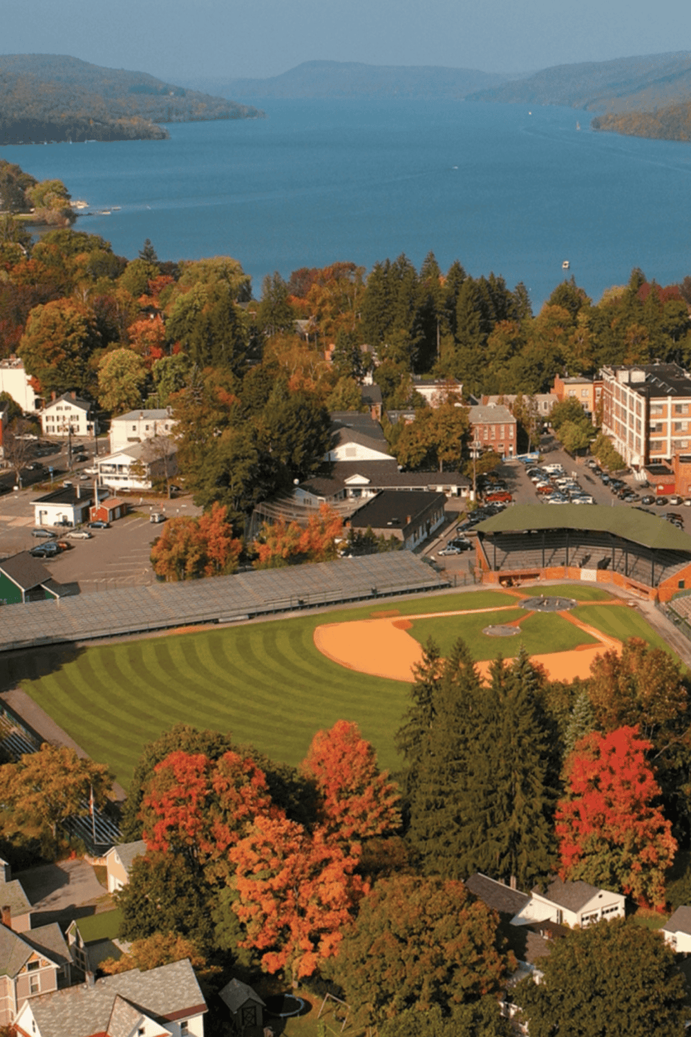 Aerial view of a lake, city, and baseball field during fall with colorful trees.