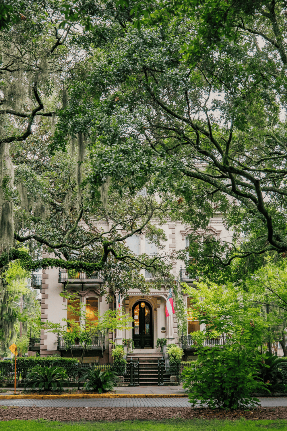 Lush greenery surrounds a historic mansion with flags, showcasing Charleston ghost tours and vacation rentals.