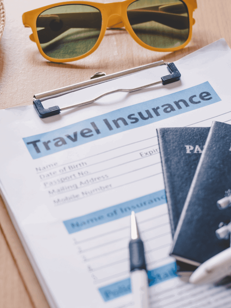 Travel insurance document with passports, sunglasses, and a pen on a wooden surface.