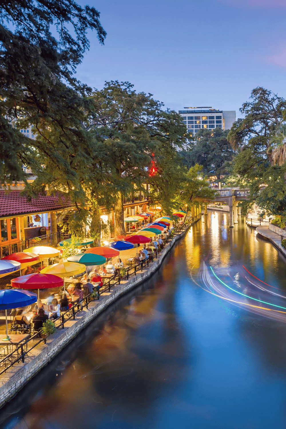Colorful riverside dining scene in San Antonio with vibrant umbrellas and lively atmosphere.