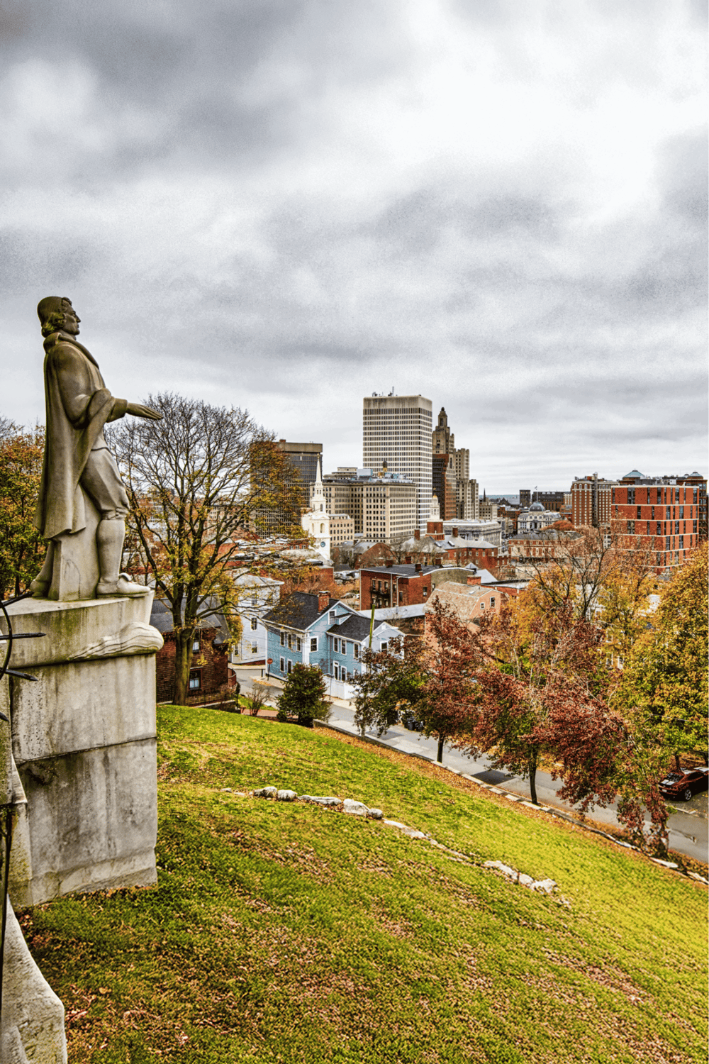 Scenic cityscape view with historic statue overlooking downtown, vibrant fall foliage, and modern buildings.