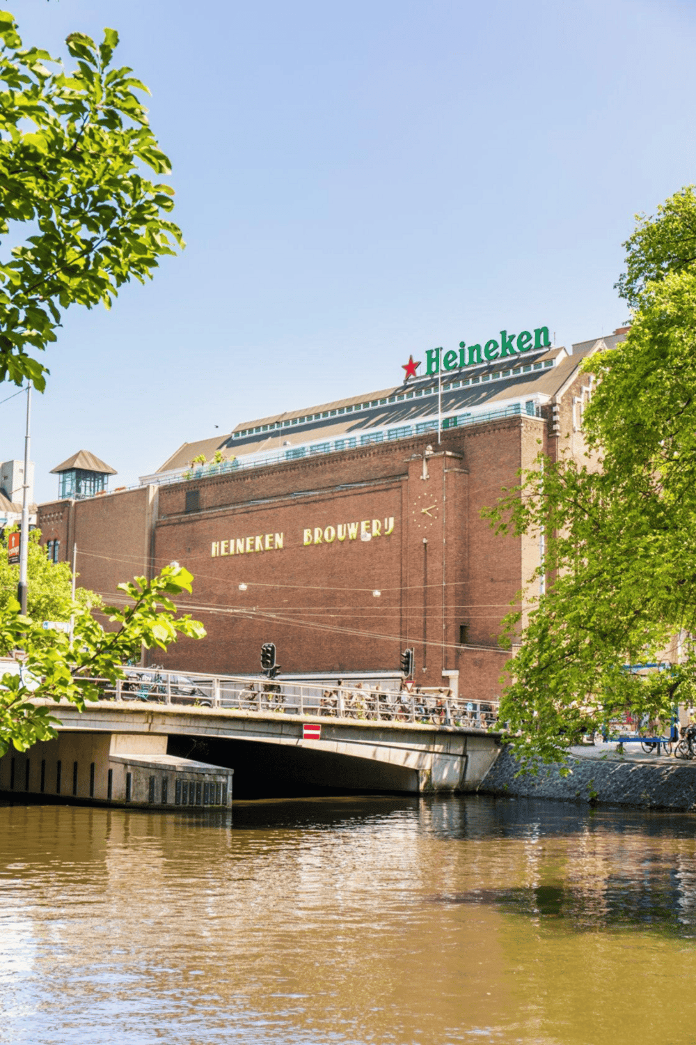 Heineken brewery building with river and lush green trees in Amsterdam, Netherlands.