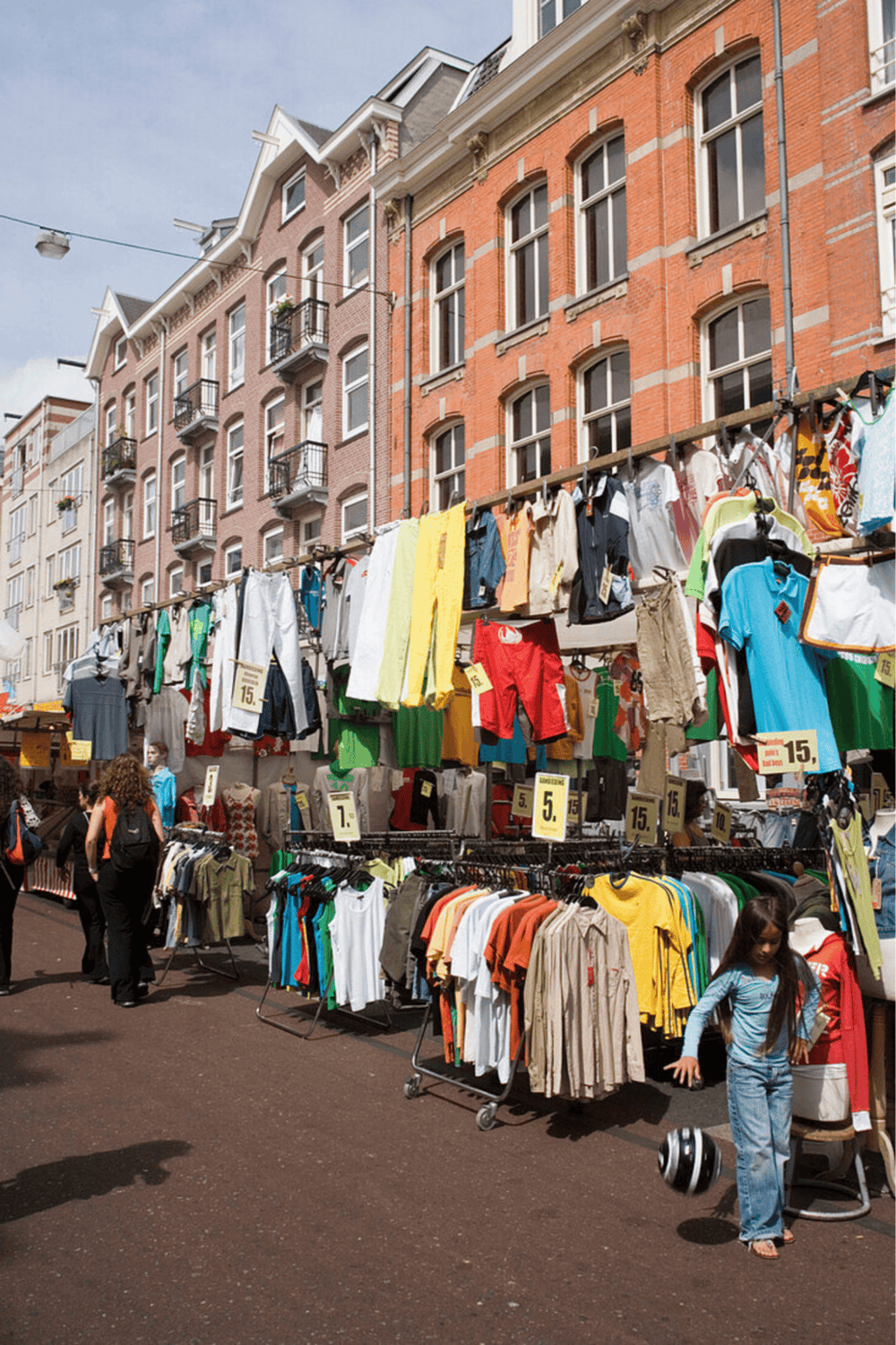 Clothing market stalls with street fashion and outdoor shopping, urban setting in front of historic brick buildings.