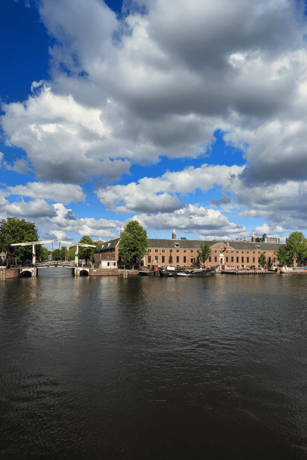 Historic canal view with bridge and brick buildings under partly cloudy sky, in a scenic cityscape.
