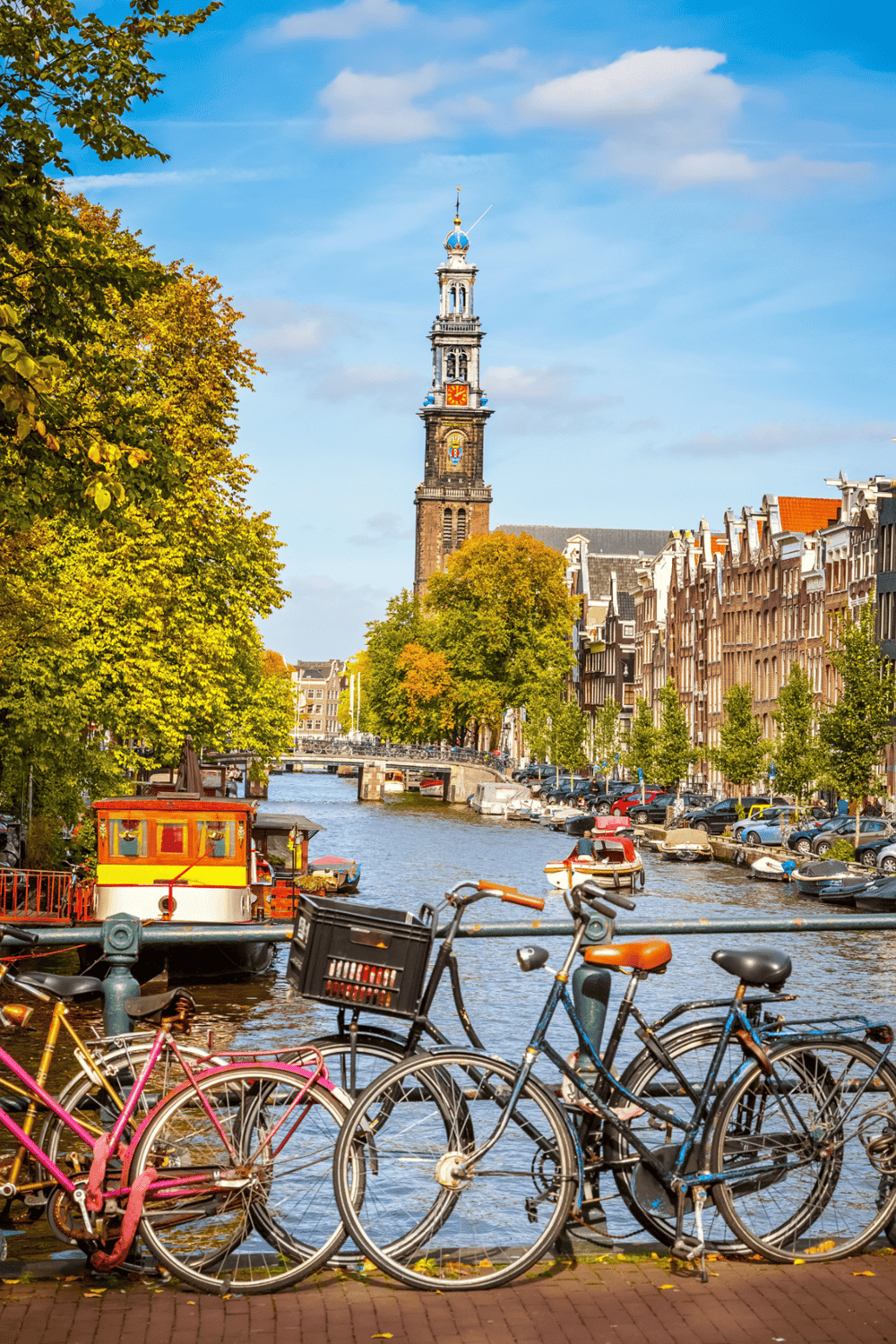 Charming Amsterdam canal with bicycles, historic buildings, and a clock tower in the background.