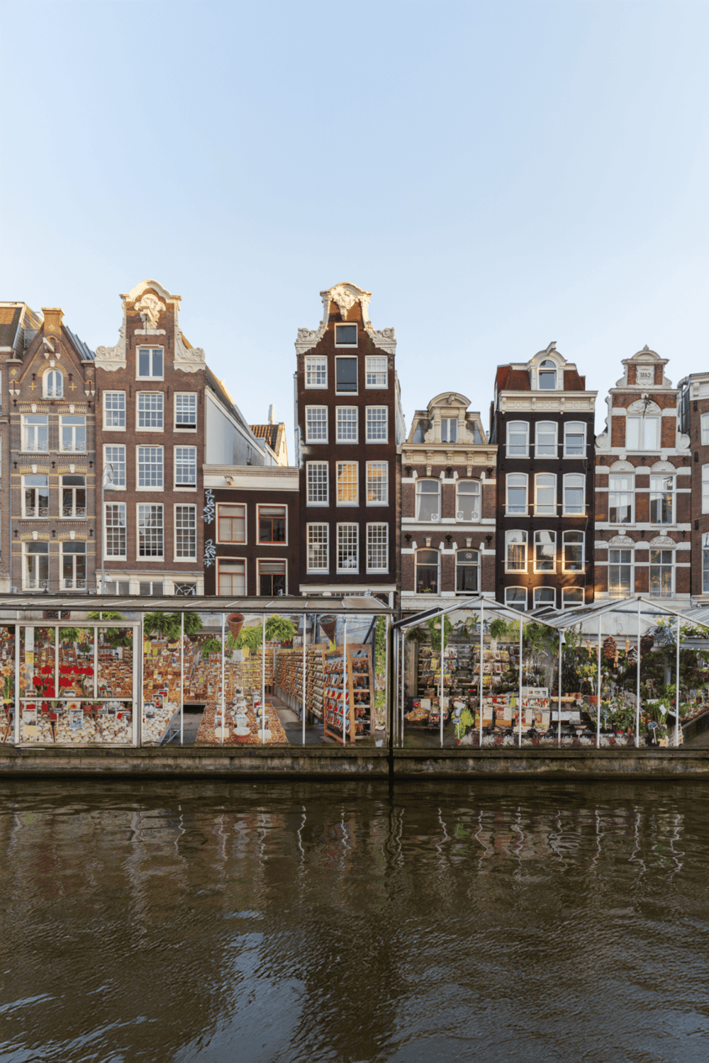 Colorful canal houses in Amsterdam with a floating flower shop, showcasing Dutch architecture and unique shopping experience.