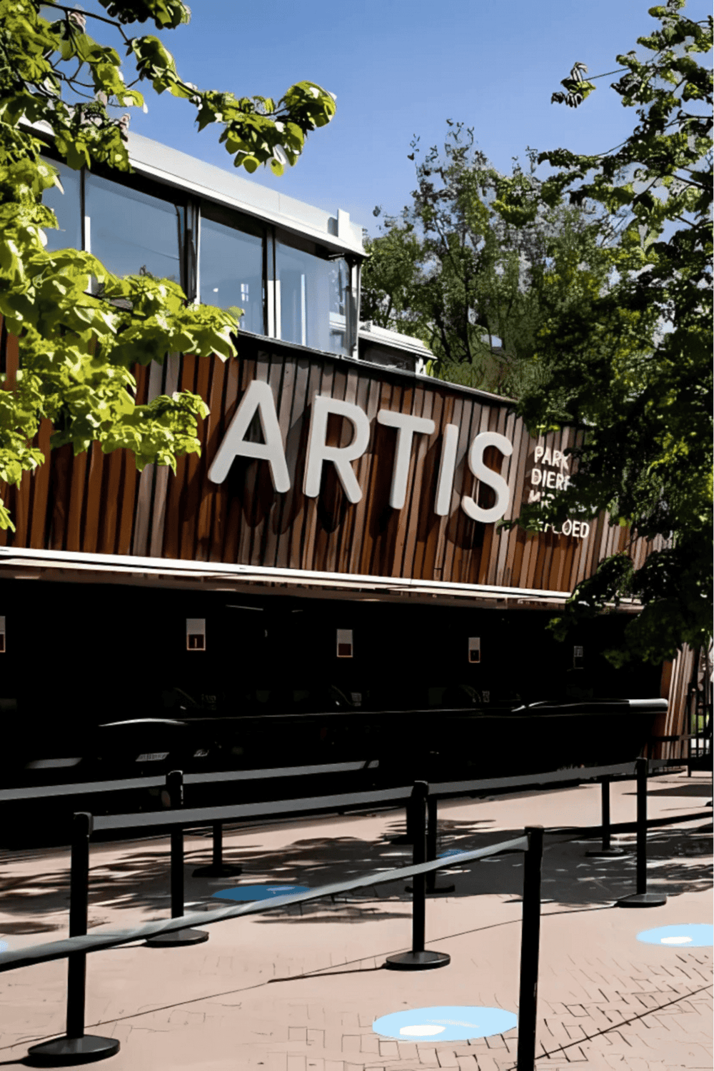 Modern arts center with wooden facade and large "ARTIS" sign, surrounded by lush trees.