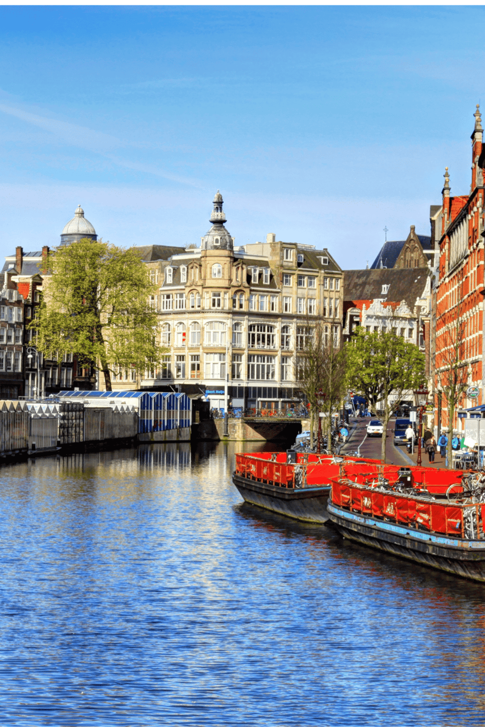 Colorful European cityscape featuring canal, boats, historic buildings, and clear blue sky.