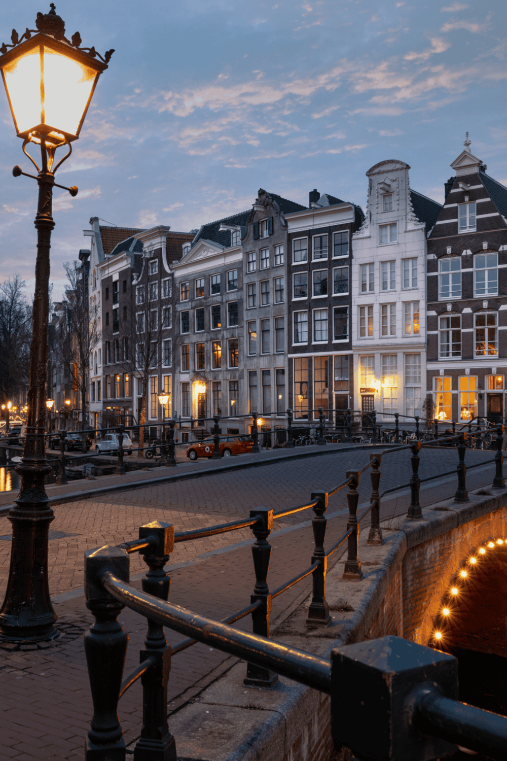 Charming canal-side street in Amsterdam with historic buildings and illuminated lamps at dusk.