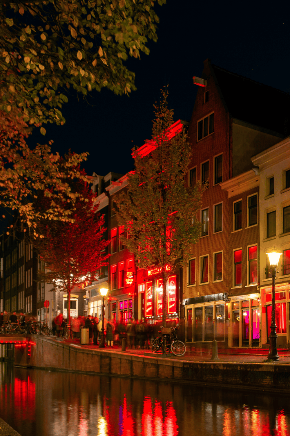 Vibrant nightlife scene in Amsterdam with illuminated red-lit bars and scenic canal views.