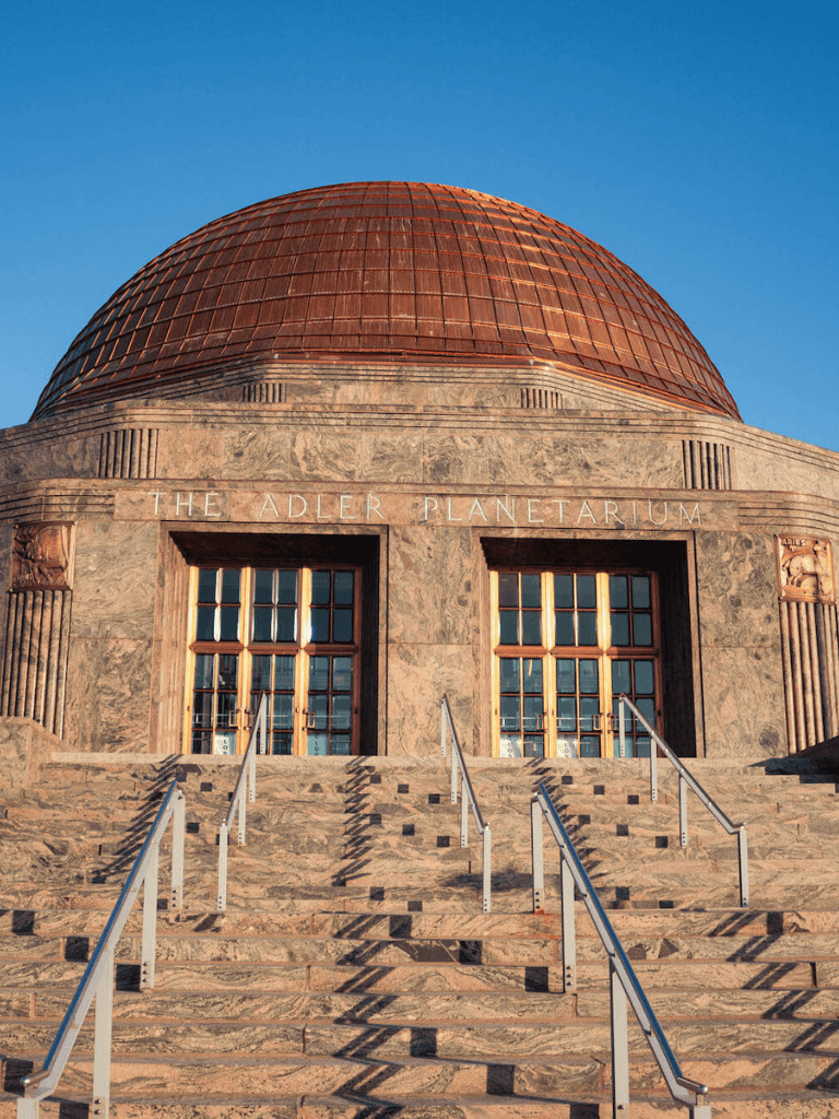 Dome-shaped Adler Planetarium building with stairs and clear blue sky, iconic Chicago science museum.