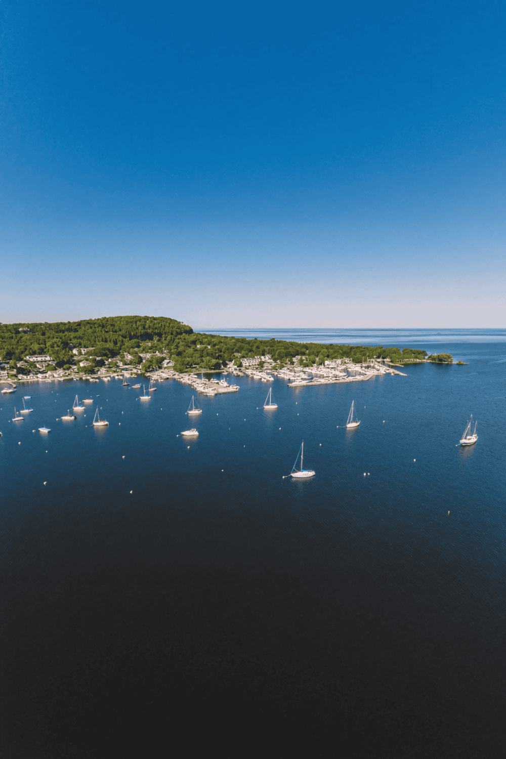 Boat marina on a calm, clear blue lake with sailboats and lush green shoreline, ideal for navigation and travel planning.
