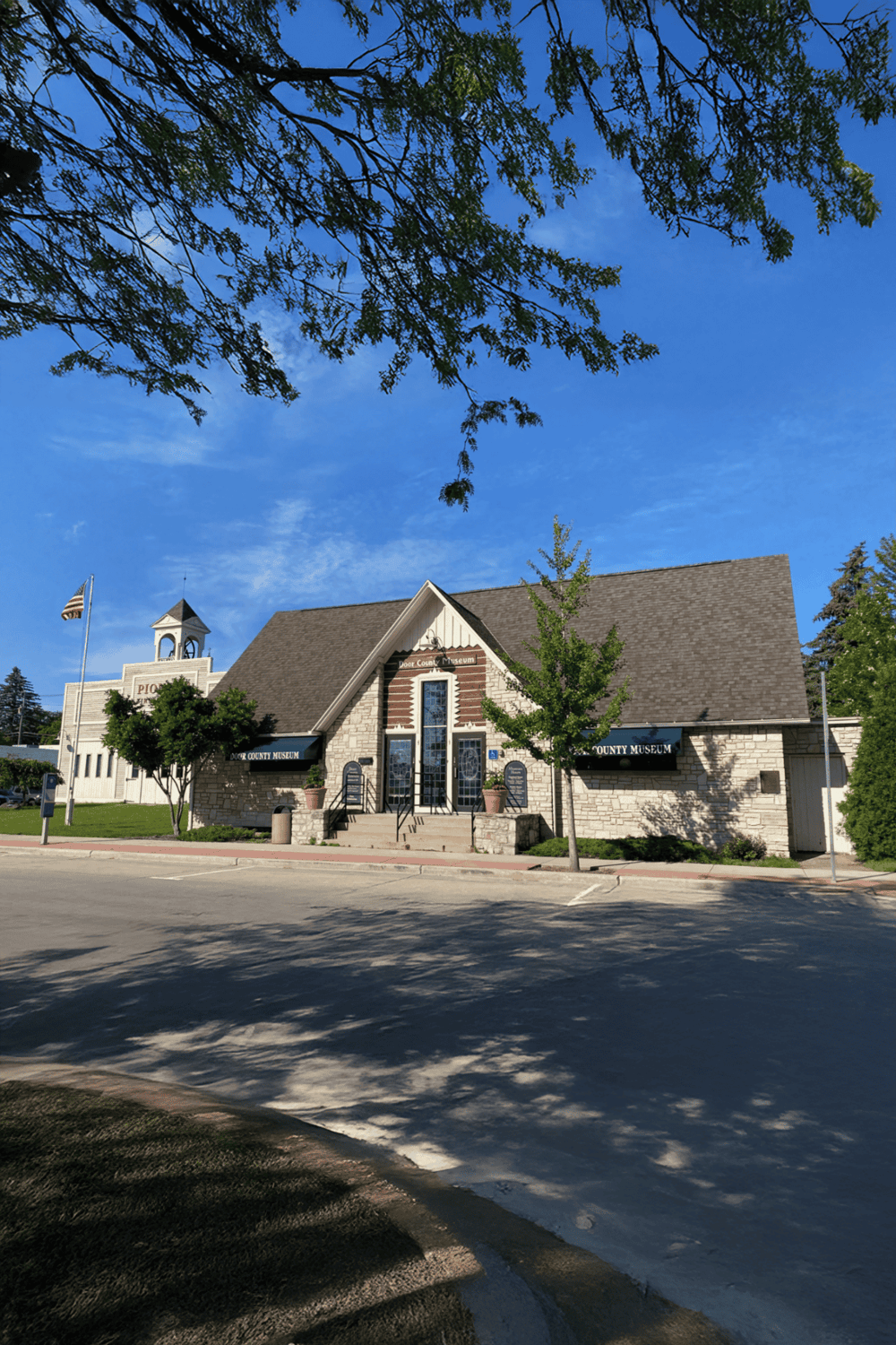 Museum building with stone exterior and flag, clear blue sky, Memorial Day flags and trees, historic architecture, downtown landscape.