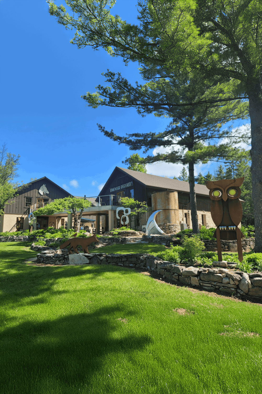 Serene outdoor scene with modern lodge, sculptures, lush greenery, and towering trees, ideal for nature and travel enthusiasts.