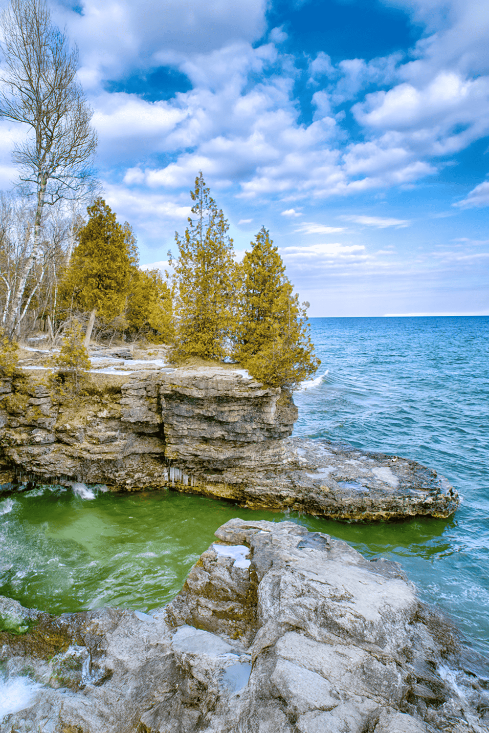 Tranquil lakeside with rocky shoreline and evergreen trees under blue sky, scenic outdoor adventure at QuestForDirections.