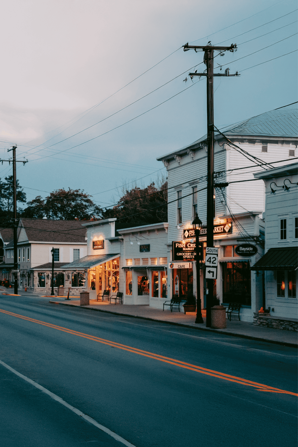 Coastal town street with shops, restaurants, and street signs, scenic seaside village at dusk.