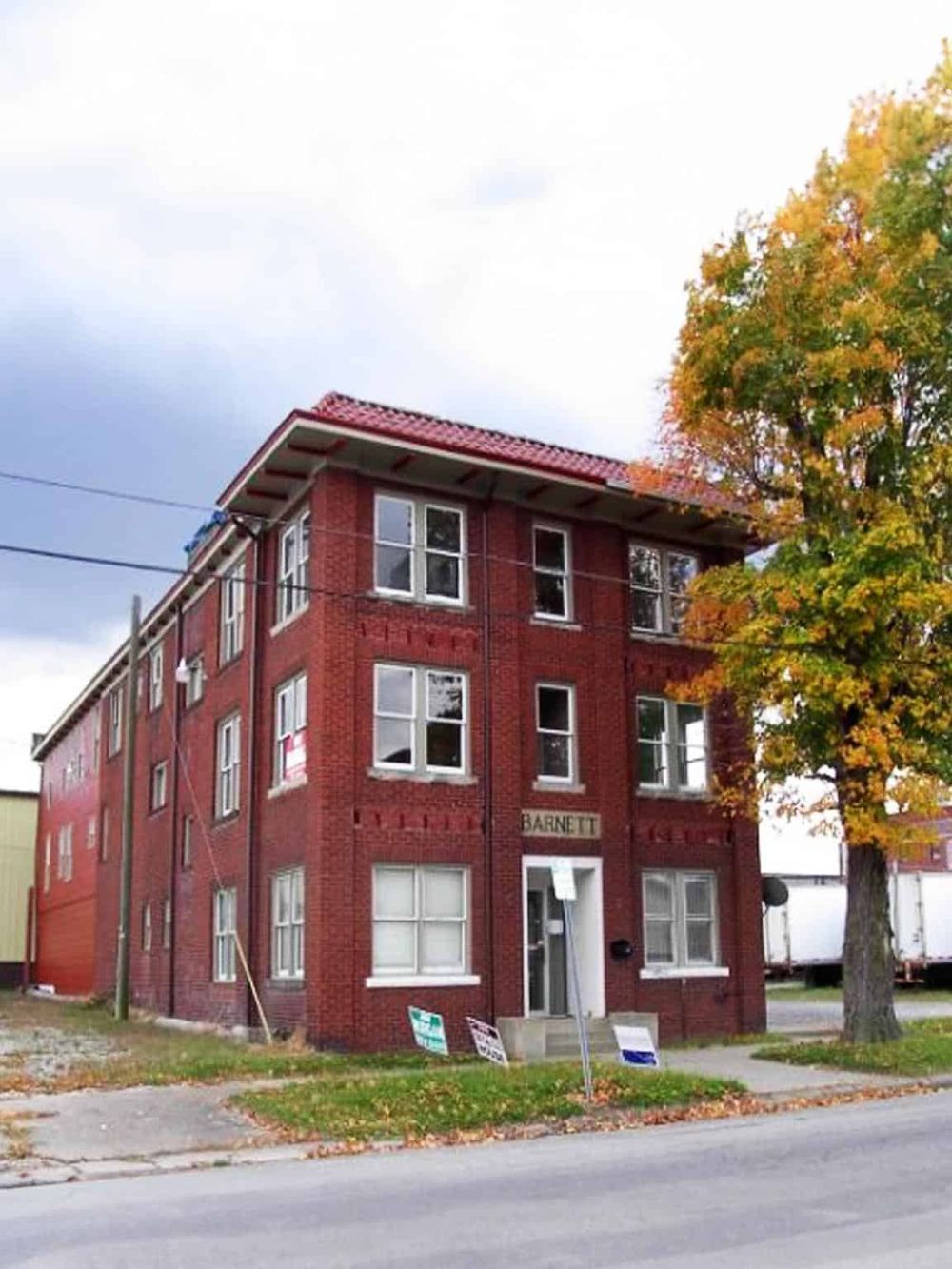 Old red brick apartment building with "Barnett" sign, surrounded by trees with fall foliage.