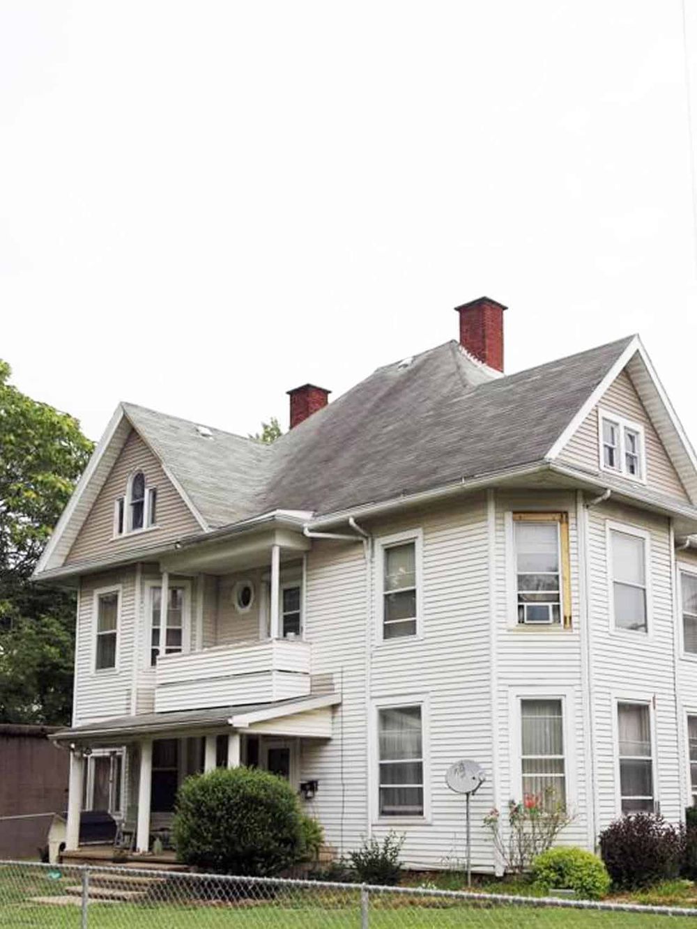 Victorian-style house with white siding, multiple windows, and a small front porch, lush garden, and satellite dish.