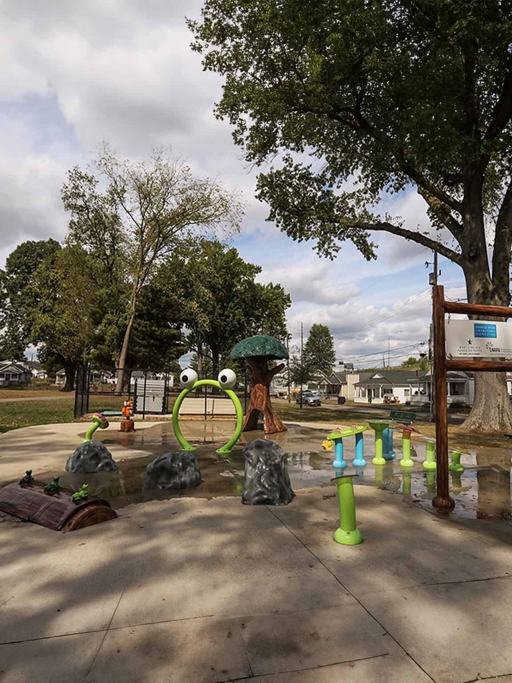 Colorful children's splash pad with frog-themed water features and playful sculptures in a park.