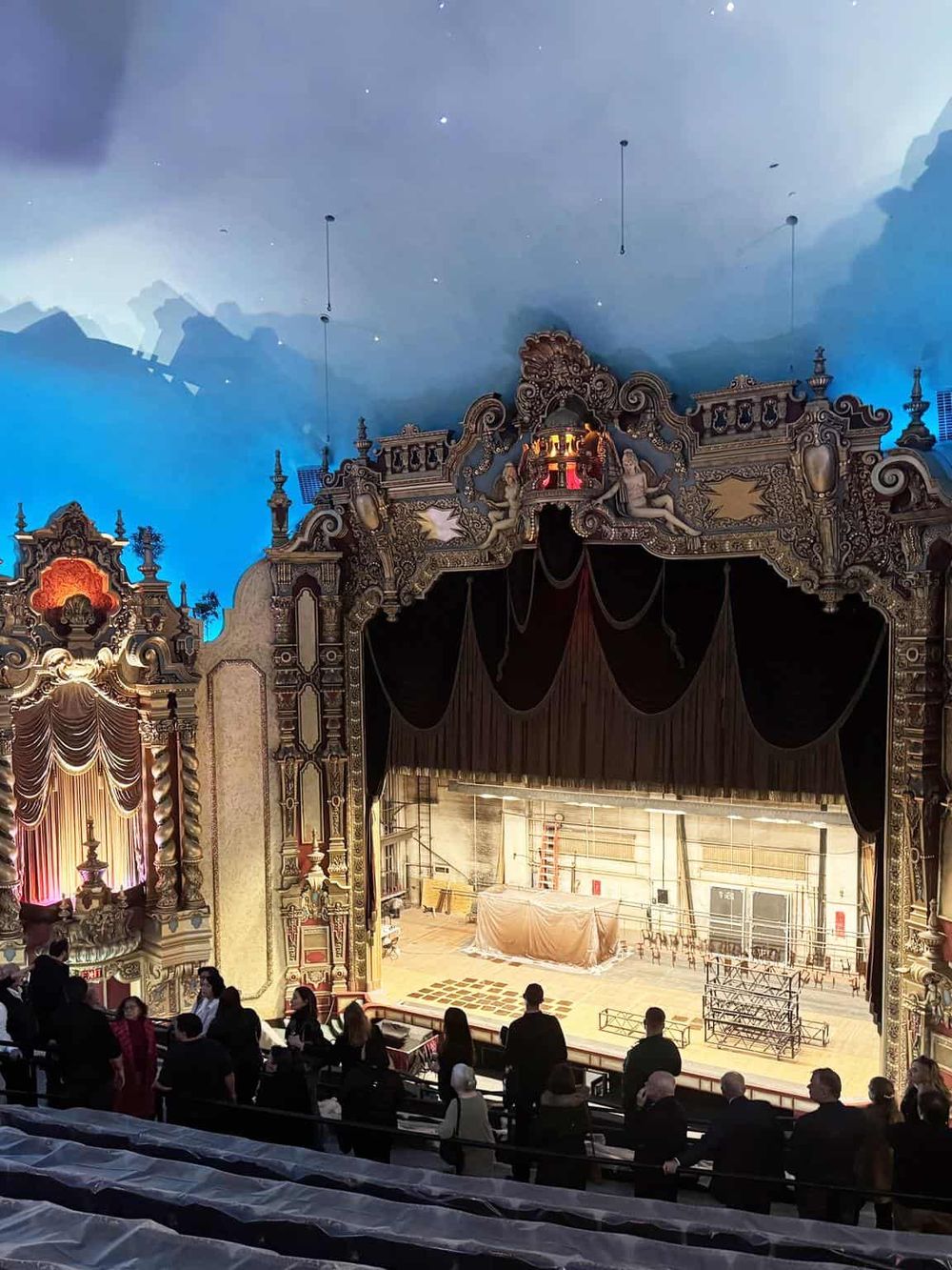 Vibrant theater stage with ornate gold carvings, black curtains, and dramatic lighting, perfect for concerts or performances.