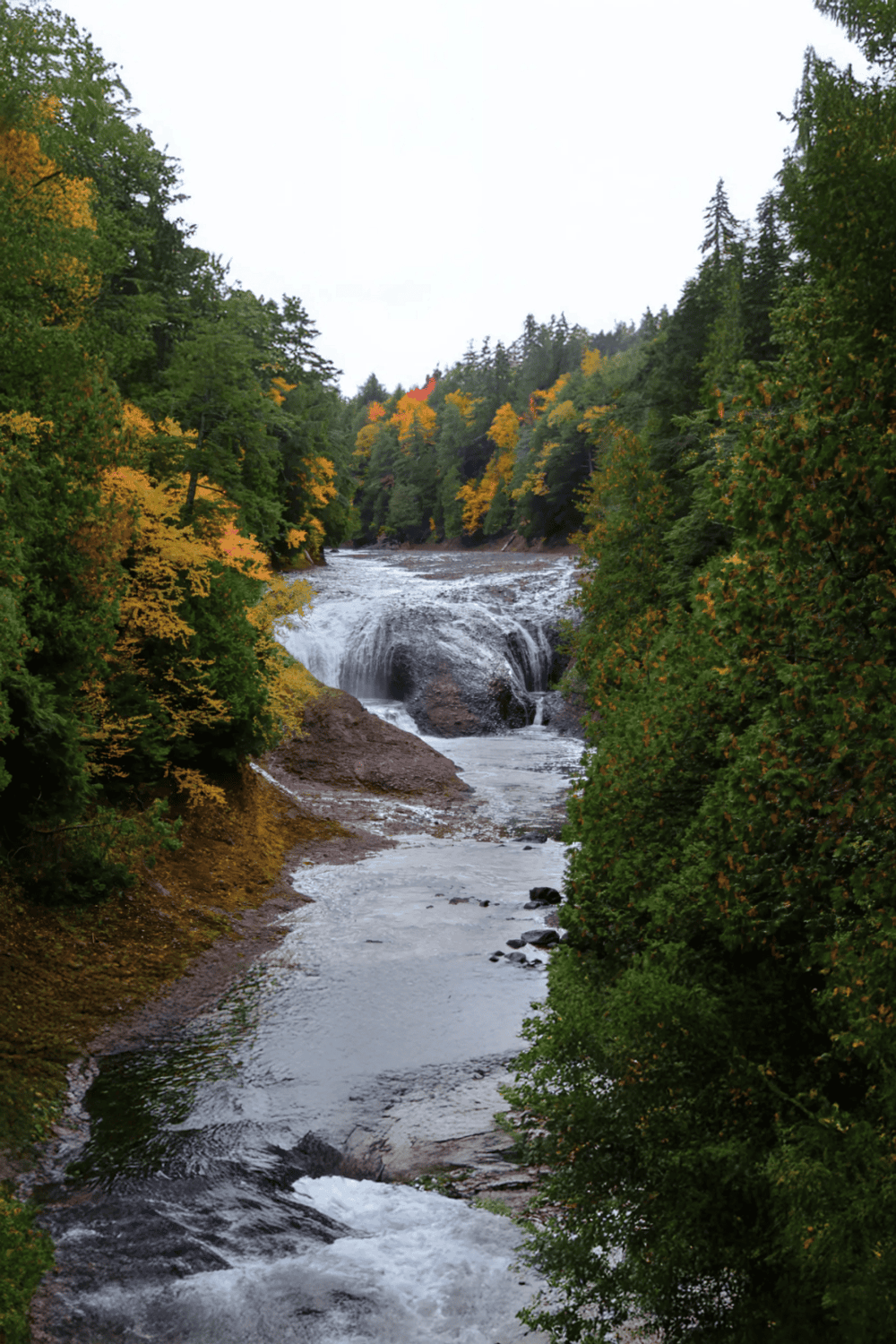 Serene river with waterfall surrounded by lush green trees, representing outdoor adventure and nature exploration.