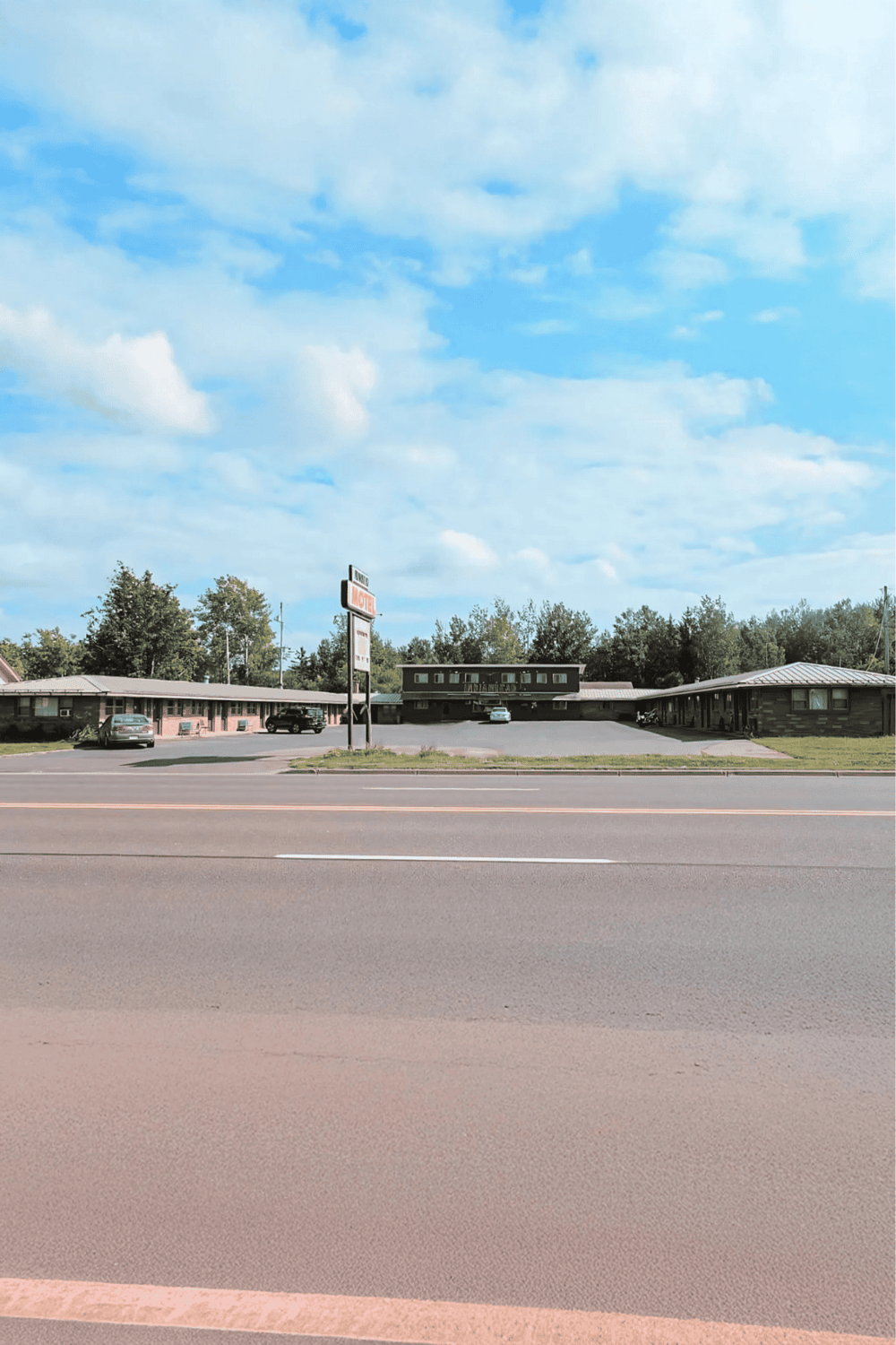 Motels near busy highway with roadside parking and large motel sign in rural area.