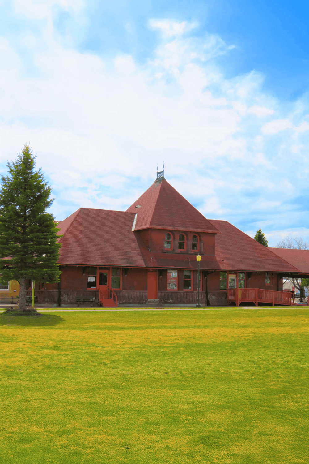 Historic red-brick building with pointed roof and bell tower in a park setting.