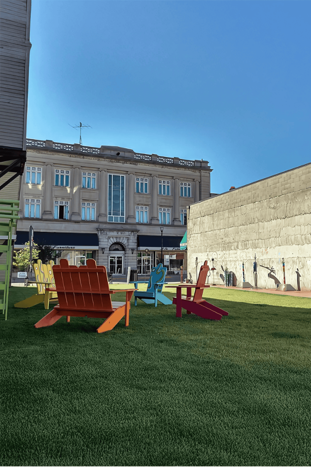 Colorful outdoor Adirondack chairs in a city park with historic buildings in the background, promoting urban relaxation and local attractions.