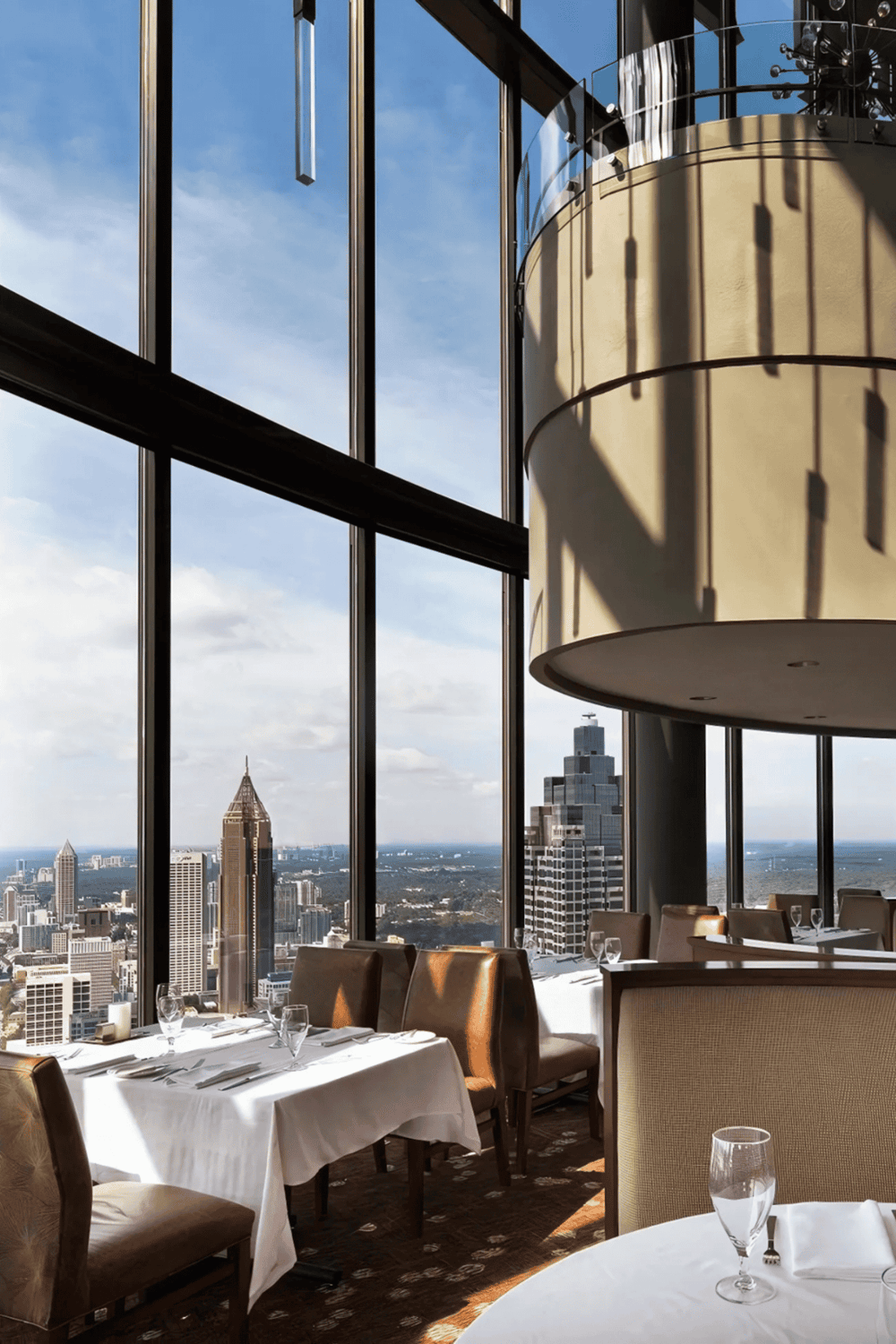 Luxury restaurant interior with panoramic city skyline views, modern decor, elegant table settings, and floor-to-ceiling windows.