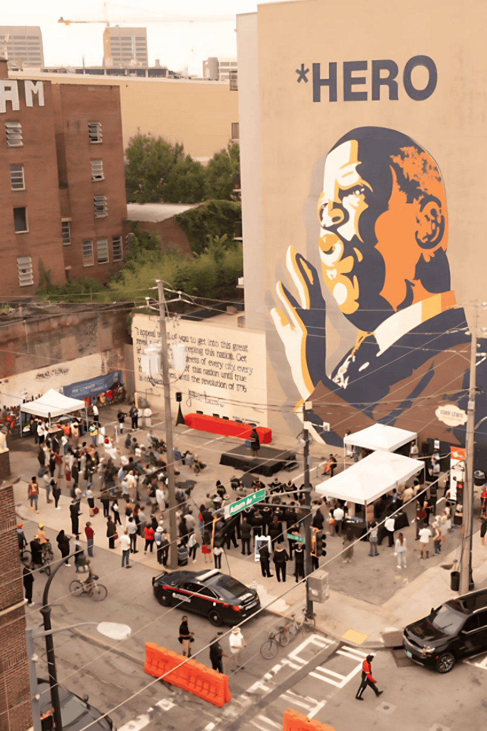 People gathered at the outdoor event with a mural of a person giving a thumbs-up, celebrating heroism and community support in the city.