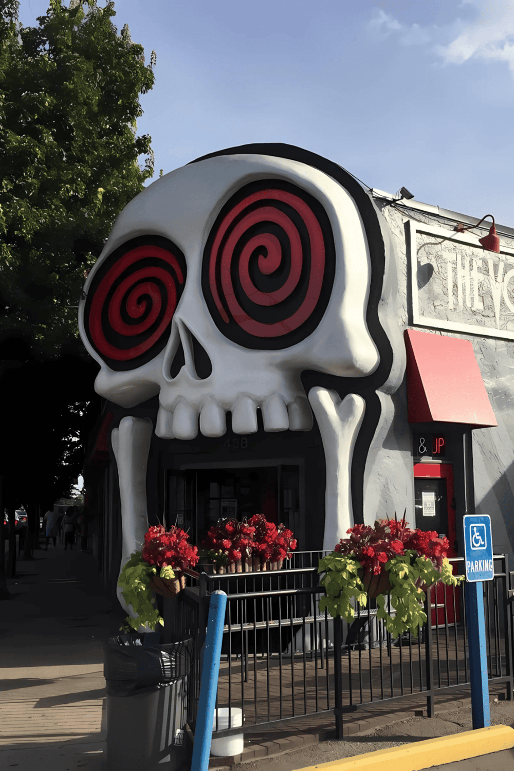 Vibrant skull-themed storefront with spiral eyes, colorful flowers, and highway parking sign.