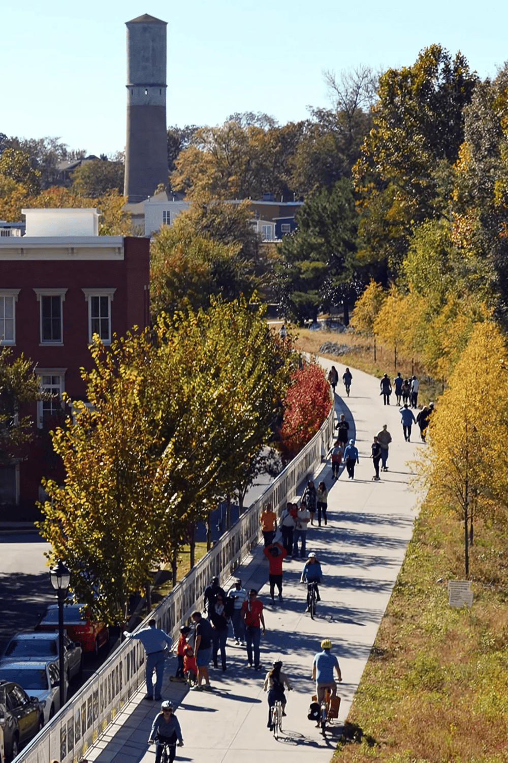 Bright autumn park path with pedestrians, cyclists, and colorful fall foliage. Community outdoor activity on a sunny day.