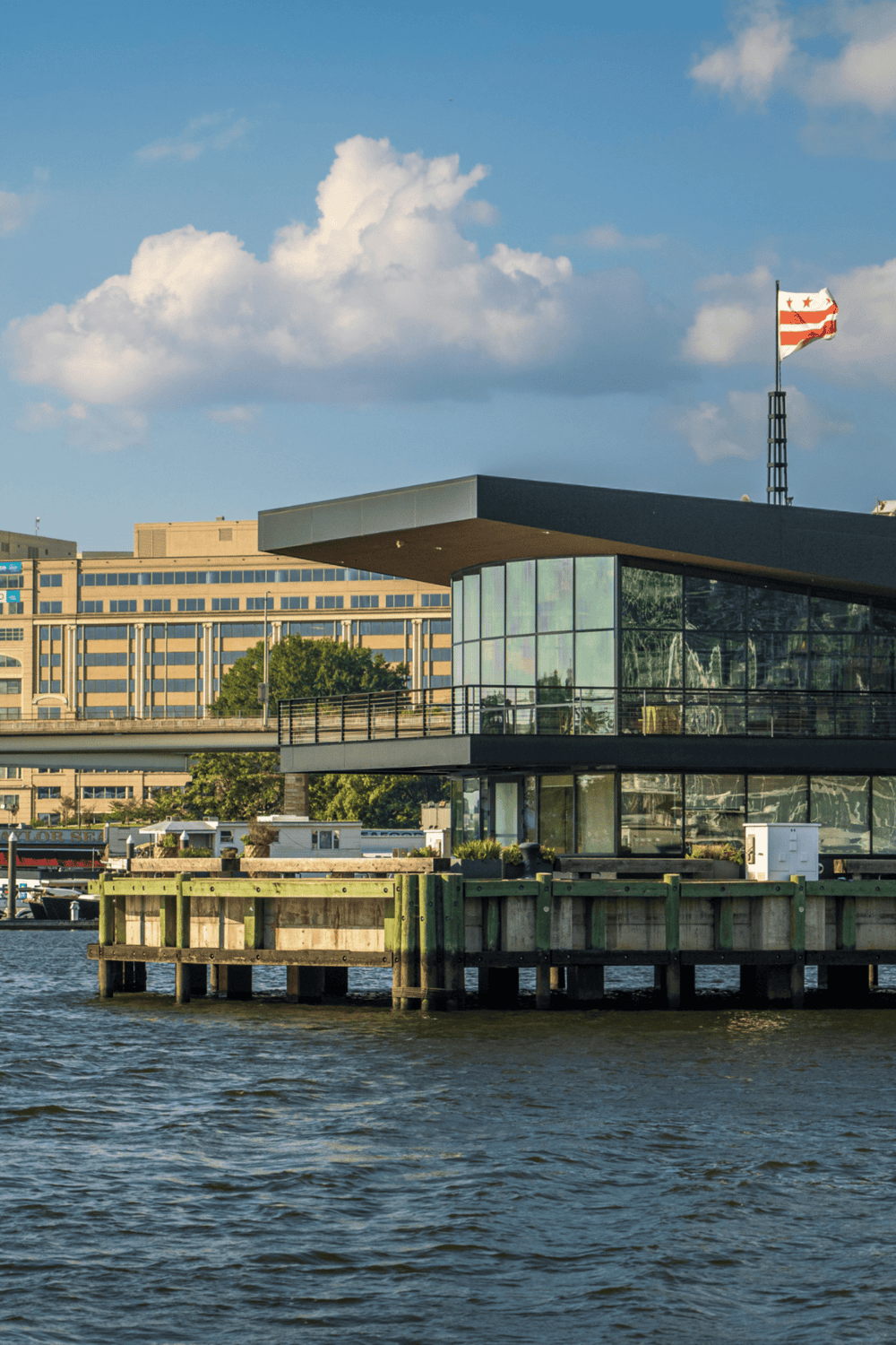 Modern waterfront building with glass facade and American flag in background.