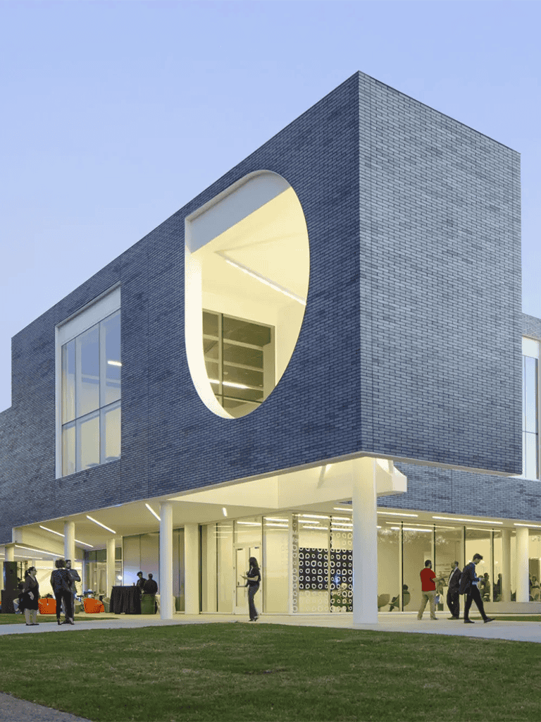 Modern university building with unique circular window, outdoor gathering, and glass front, showcasing innovative architecture.