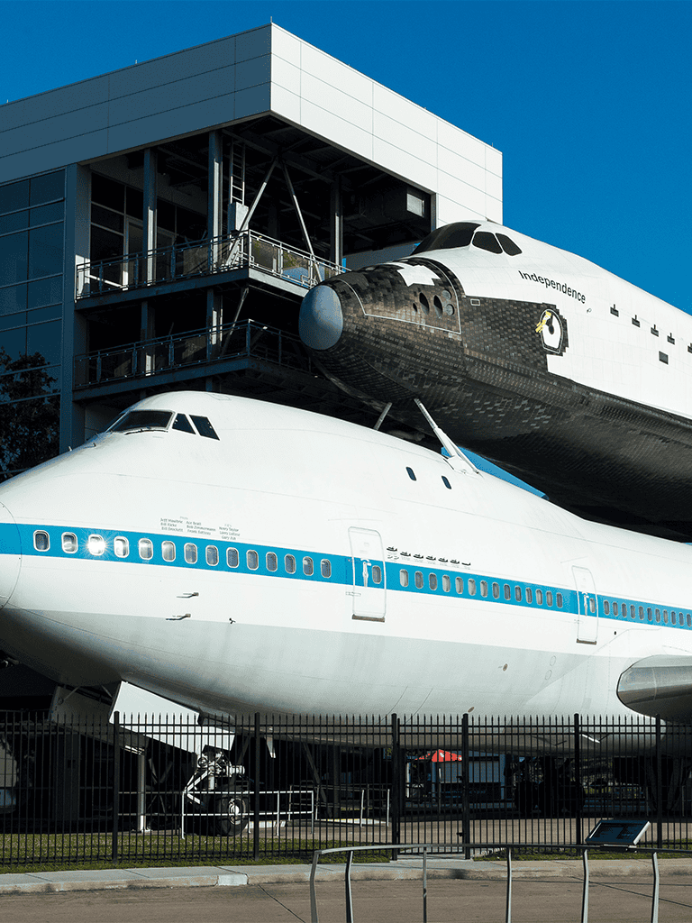 Vintage space shuttle on display at a museum with modern building in the background.