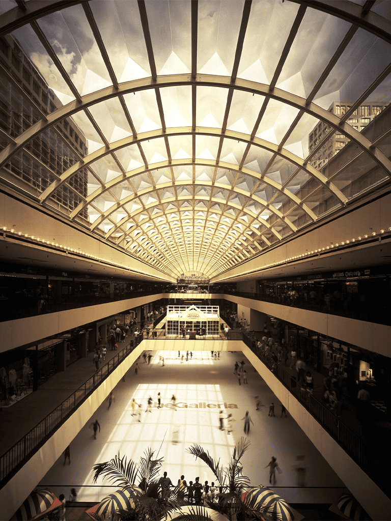 Vibrant shopping mall with glass ceiling, bustling ice skating rink, and modern architecture.