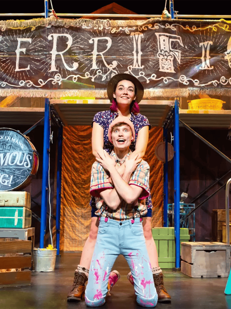 Bright theatrical performers at a magic show, with a "FRIEND" sign in the background, showcasing entertainment and fun.